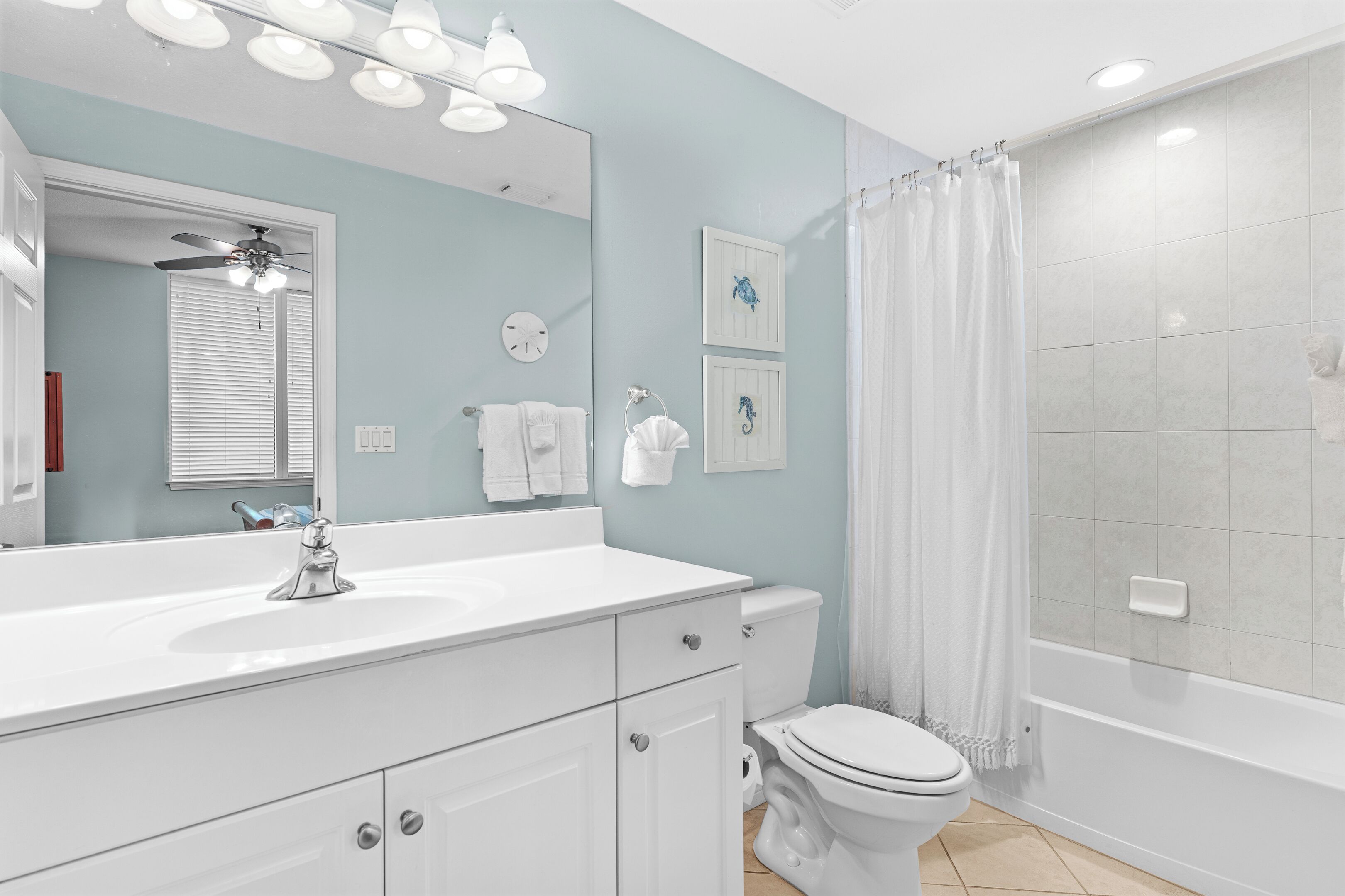 A modern bathroom with a white vanity, a toilet, a shower with a curtain, and a ceiling fan.