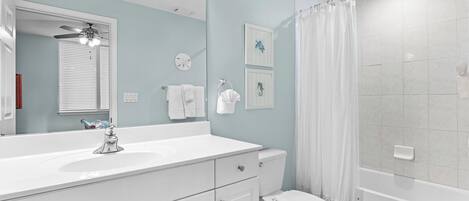 A modern bathroom with a white vanity, a toilet, a shower with a curtain, and a ceiling fan.