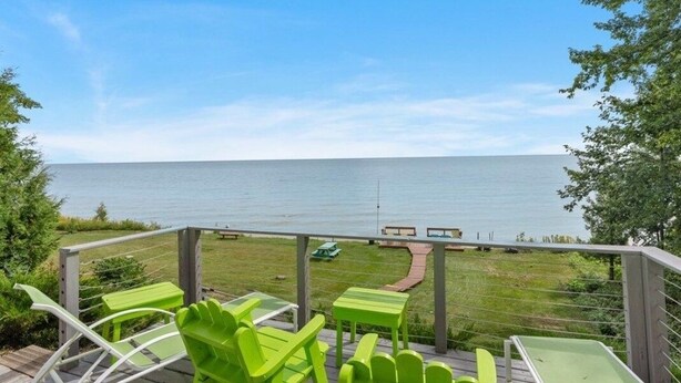 A deck with green chairs and tables overlooking a body of water.