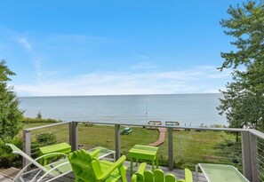 A deck with green chairs and tables overlooking a body of water.