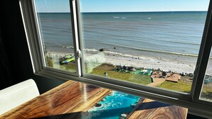 A view of the ocean through a window, with a wooden table in the foreground.