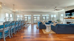 A spacious living room with a long dining table, blue sofas, and a fireplace. - Sunrise Manor,  Putting Green, Pool/hot tub, Elevator, Ocean Views (Isle of Palms)
