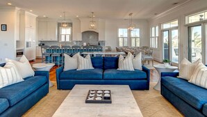 A spacious living room with a blue sofa set, a coffee table, and a kitchen in the background. - Sunrise Manor,  Putting Green, Pool/hot tub, Elevator, Ocean Views (Isle of Palms)