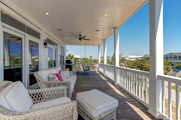 A covered outdoor area with wicker furniture, a ceiling fan, and a view of the surrounding landscape.