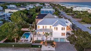 A large white house with a pool, multiple balconies, and a view of the ocean.