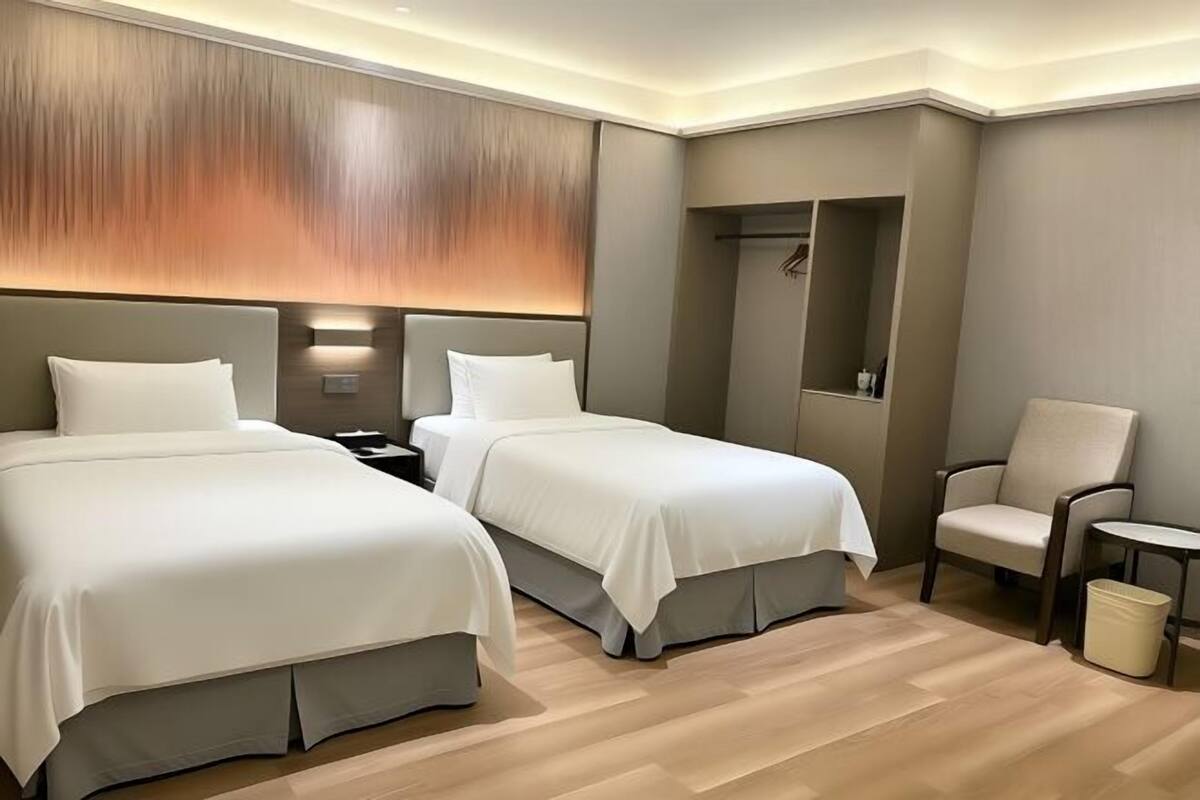A hotel room with two beds, a chair, a small table, and a walk-in closet.