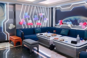 Een moderne kamer met een blauwe bank, een klein oranje stoeltje, een grijze bank en een toonbank met verschillende spullen.