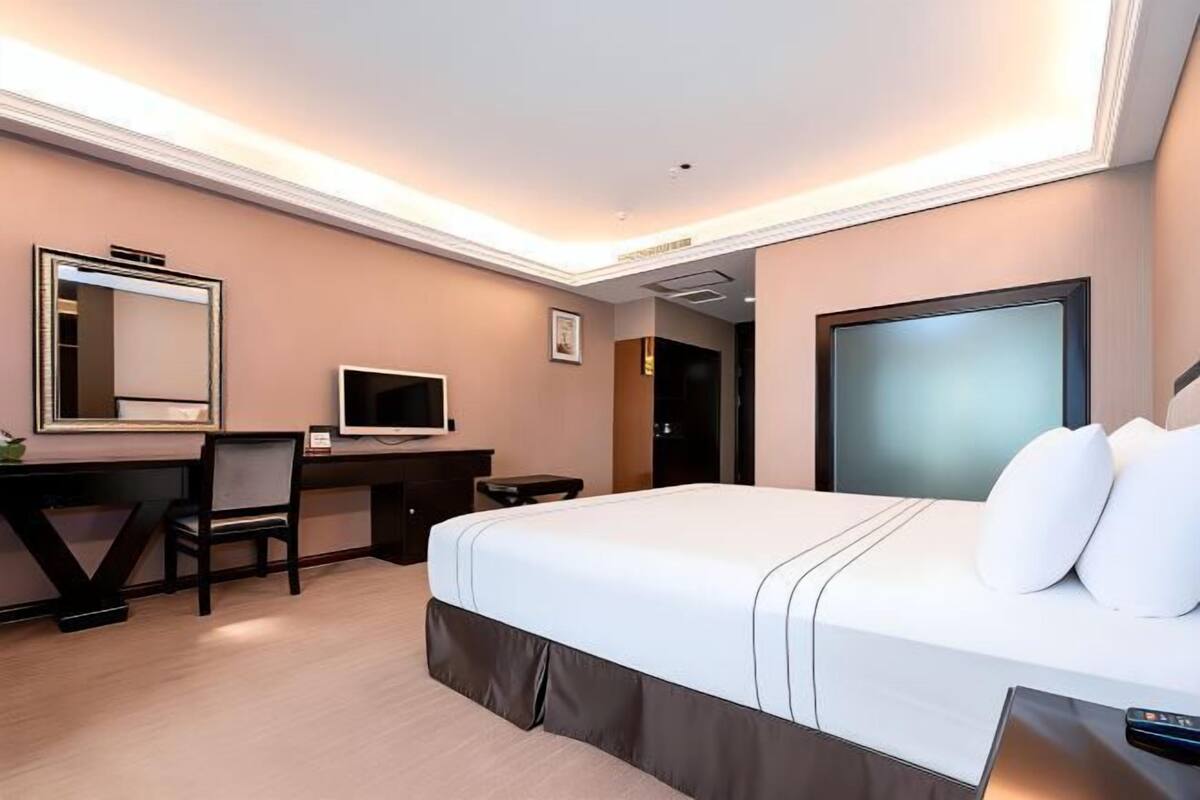 A hotel room with a large bed, a desk with a computer, a television, and a mirror.