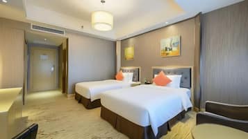 A hotel room with two beds, a sitting area, and a door leading to a hallway.