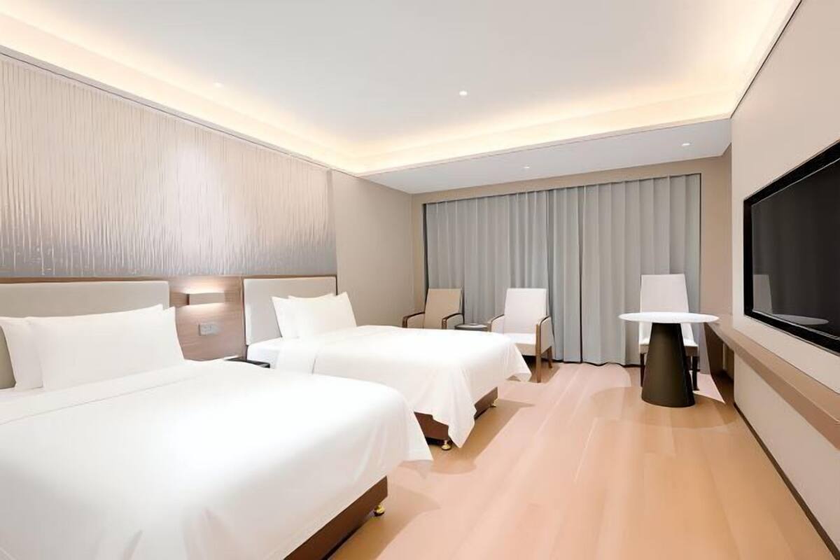 A hotel room with two beds, a TV, a table, and a window.