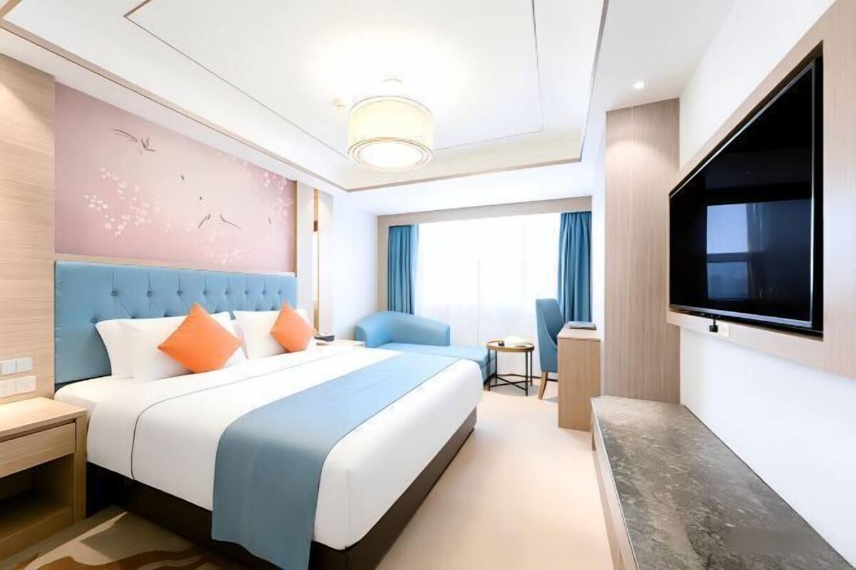 A modern hotel room with a large bed, a desk, a chair, a TV, and a window with curtains.