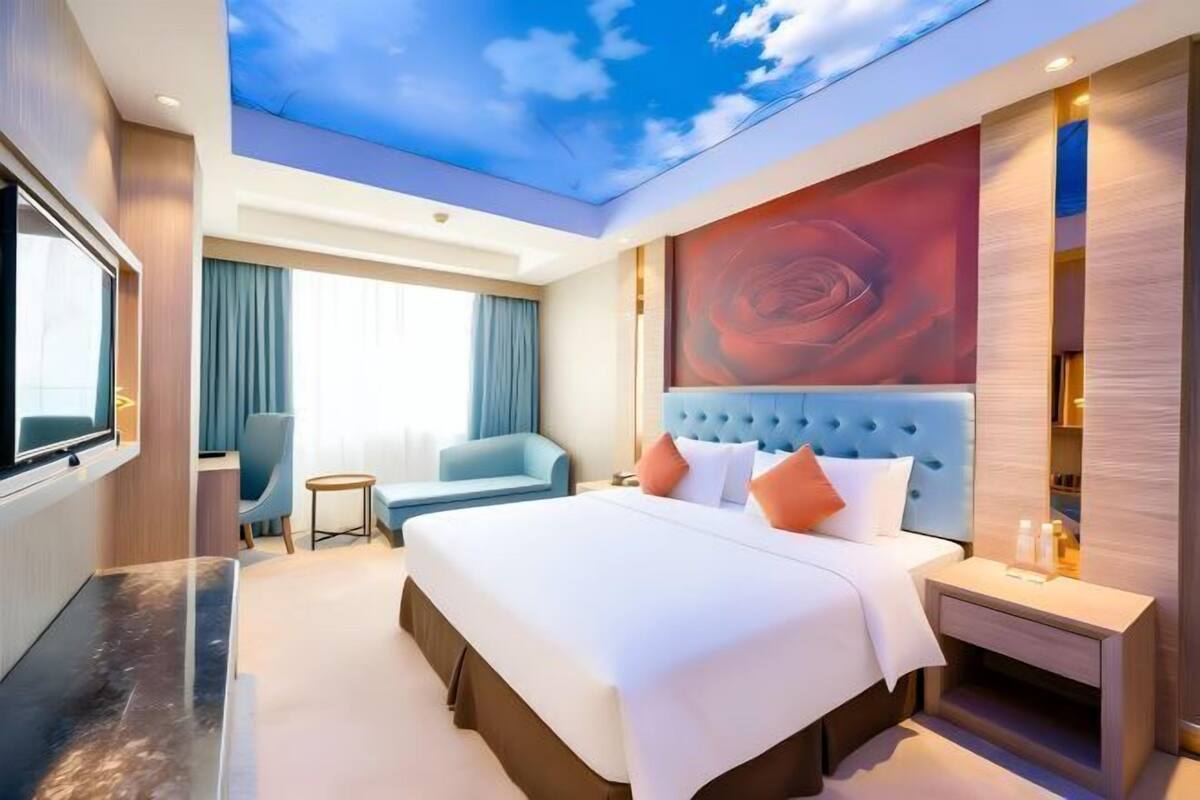 A modern hotel room with a large bed, a television, a seating area, and a ceiling mural.