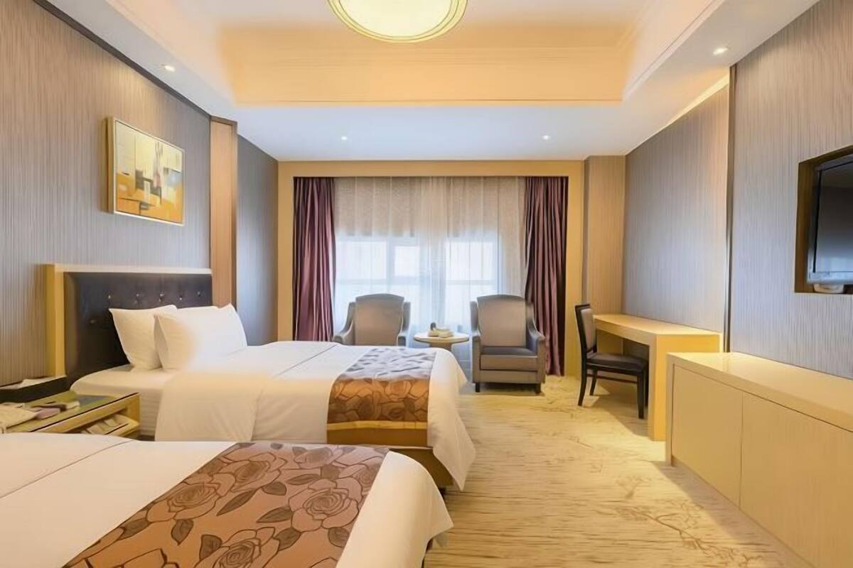 A hotel room with two beds, a desk, chairs, and a TV.