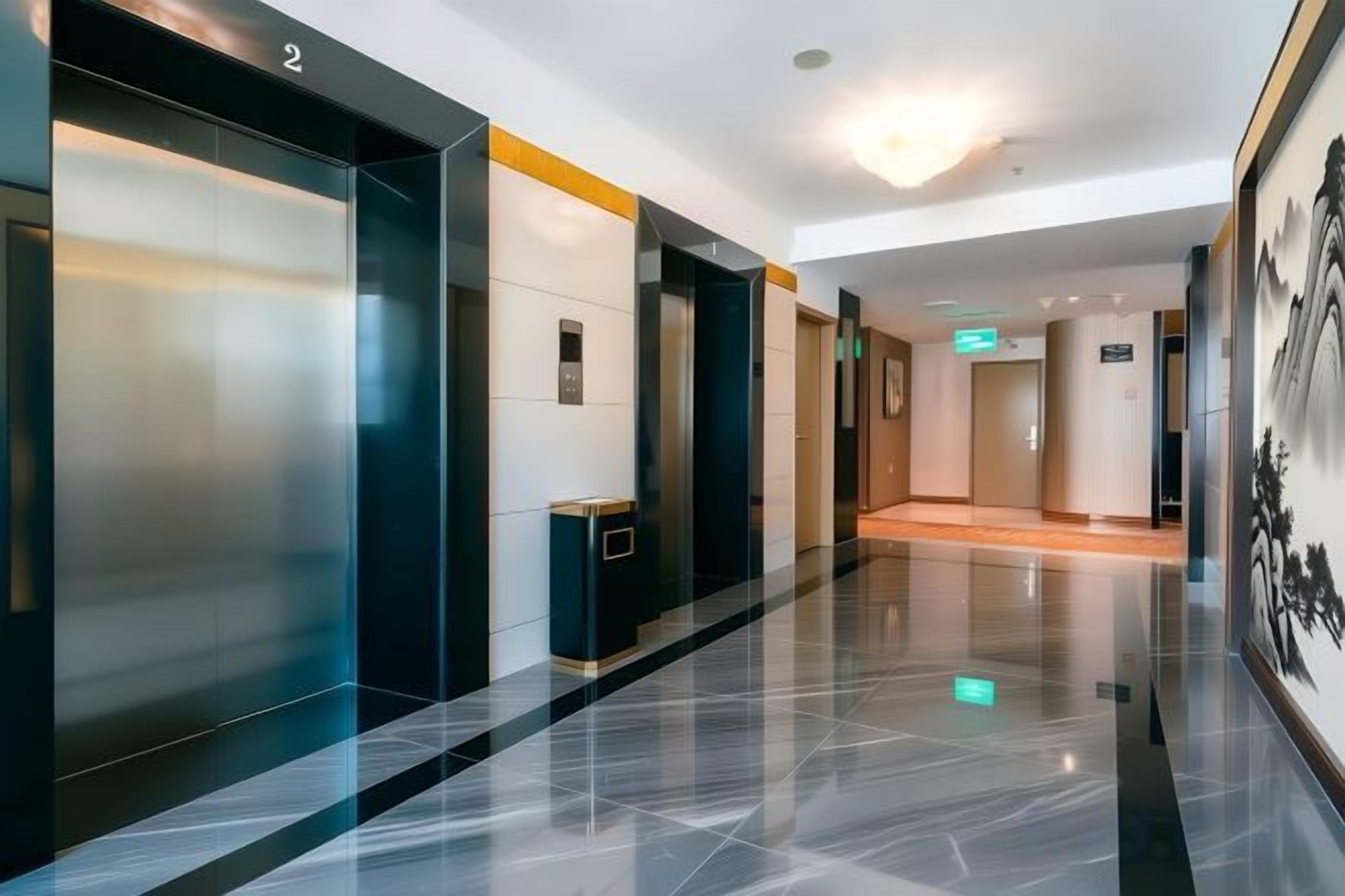A modern hotel lobby with a polished floor, elevators, and a corridor leading to rooms.
