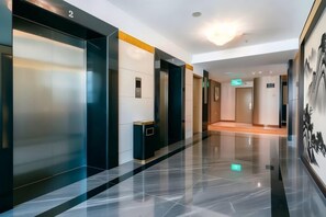 A modern hotel lobby with a polished floor, elevators, and a corridor leading to rooms. - Oriental Paris Business Hotel (Shishi)