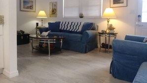 A living room with a blue sofa, a round coffee table, two lamps, and a window with blinds. - WATERFRONT COTTAGE w/ACCESS TO WEEKI WACHEE RIVER & GULF FRESHLY REMODELED! (Weeki Wachee)
