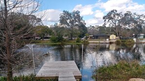 A wooden dock extending into a calm lake surrounded by trees and a few buildings in the background. - WATERFRONT COTTAGE w/ACCESS TO WEEKI WACHEE RIVER & GULF FRESHLY REMODELED! (Weeki Wachee)