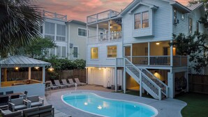 Une maison à deux étages avec une piscine dans le jardin, un espace salon extérieur et une terrasse couverte.