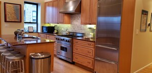 Una cocina con armarios de madera, electrodomésticos de acero inoxidable, una estufa a gas y un refrigerador.