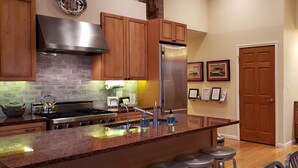 Una cocina moderna con armarios de madera, electrodomésticos de acero inoxidable, un salpicadero de ladrillo y una isla grande con taburetes de bar.