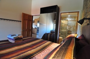 Un dormitorio con cama, armario y baño visible a través de una puerta abierta.