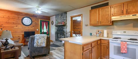 Una cocina acogedora con armarios de madera, una chimenea de piedra, un comedor con mesa y sillas, y una sala de estar con sofá y televisor.