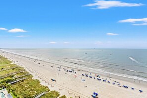 A beach with a long stretch of sand, a few umbrellas, and a clear sky.
