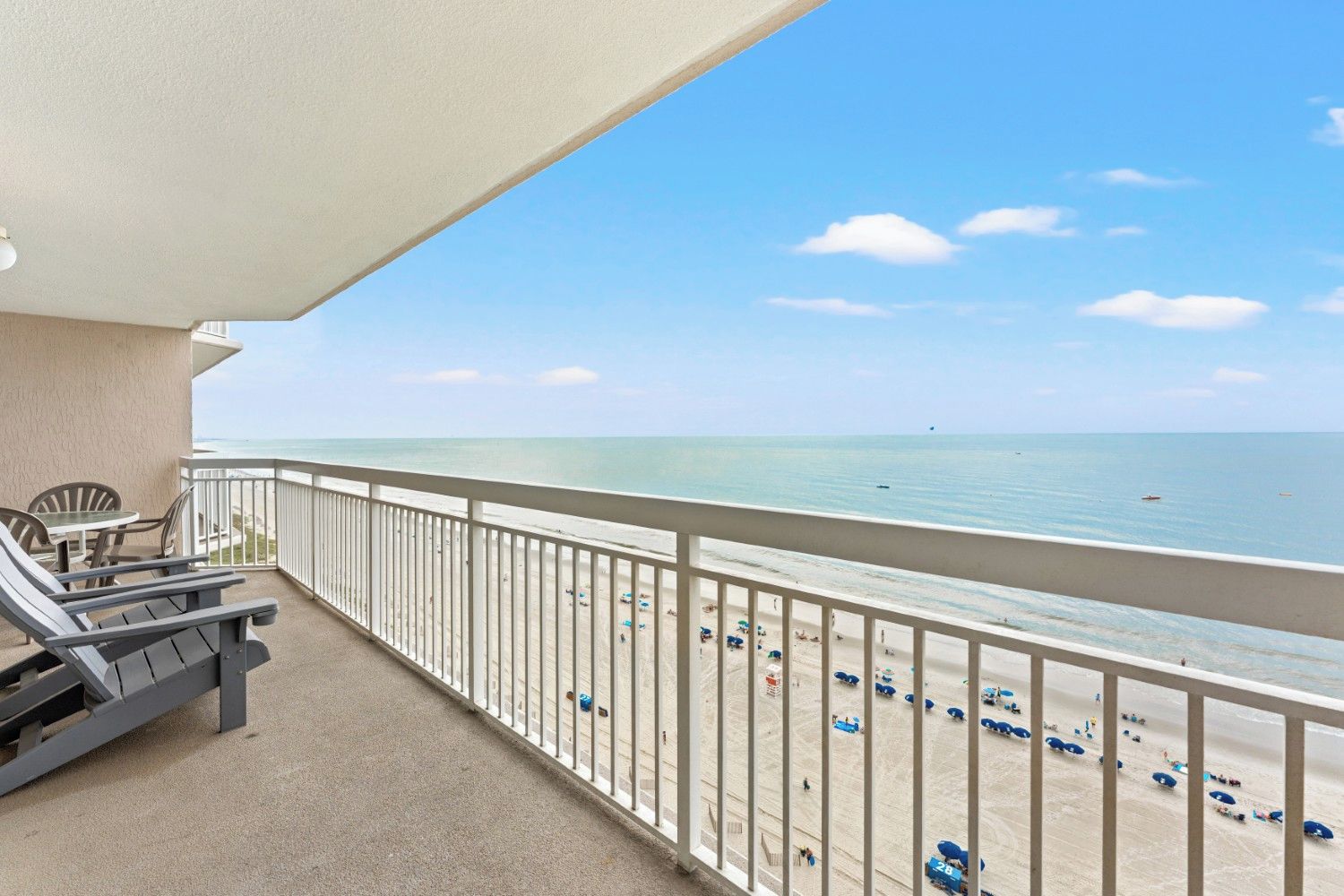 A balcony with a view of the beach, a table with chairs, and a railing.
