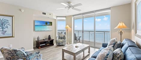 A spacious living room with a large window, a ceiling fan, and a view of the ocean.