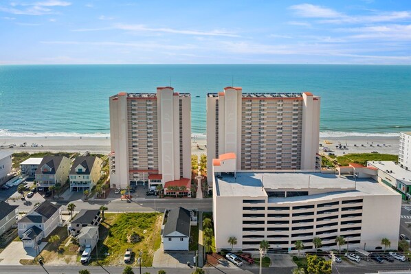 Un hotel costero con dos edificios altos, un estacionamiento y vistas a la playa.