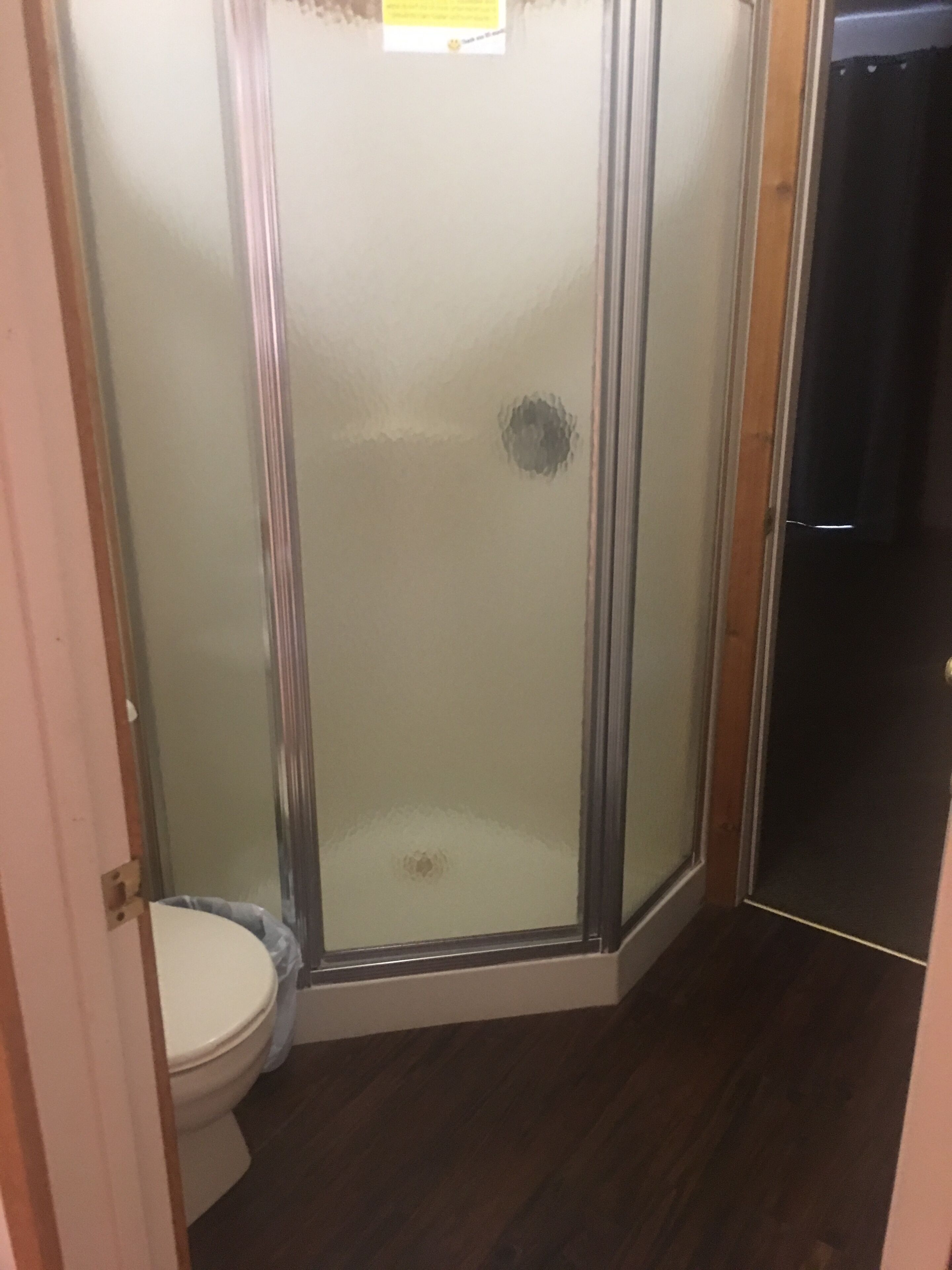 Un baño con cabina de ducha de vidrio, inodoro y suelo de madera oscura.