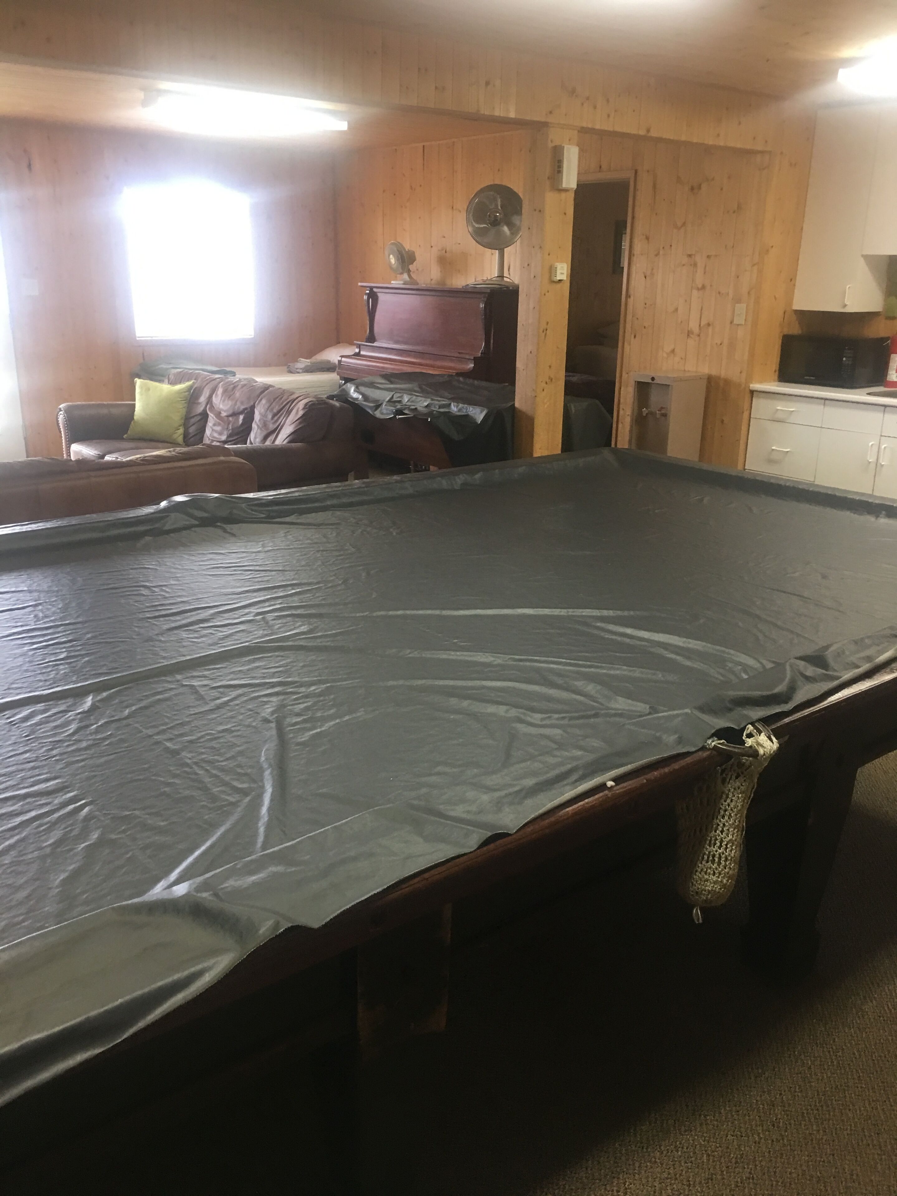 A room with a pool table, a wooden ceiling, a window, and a microwave on a cabinet.