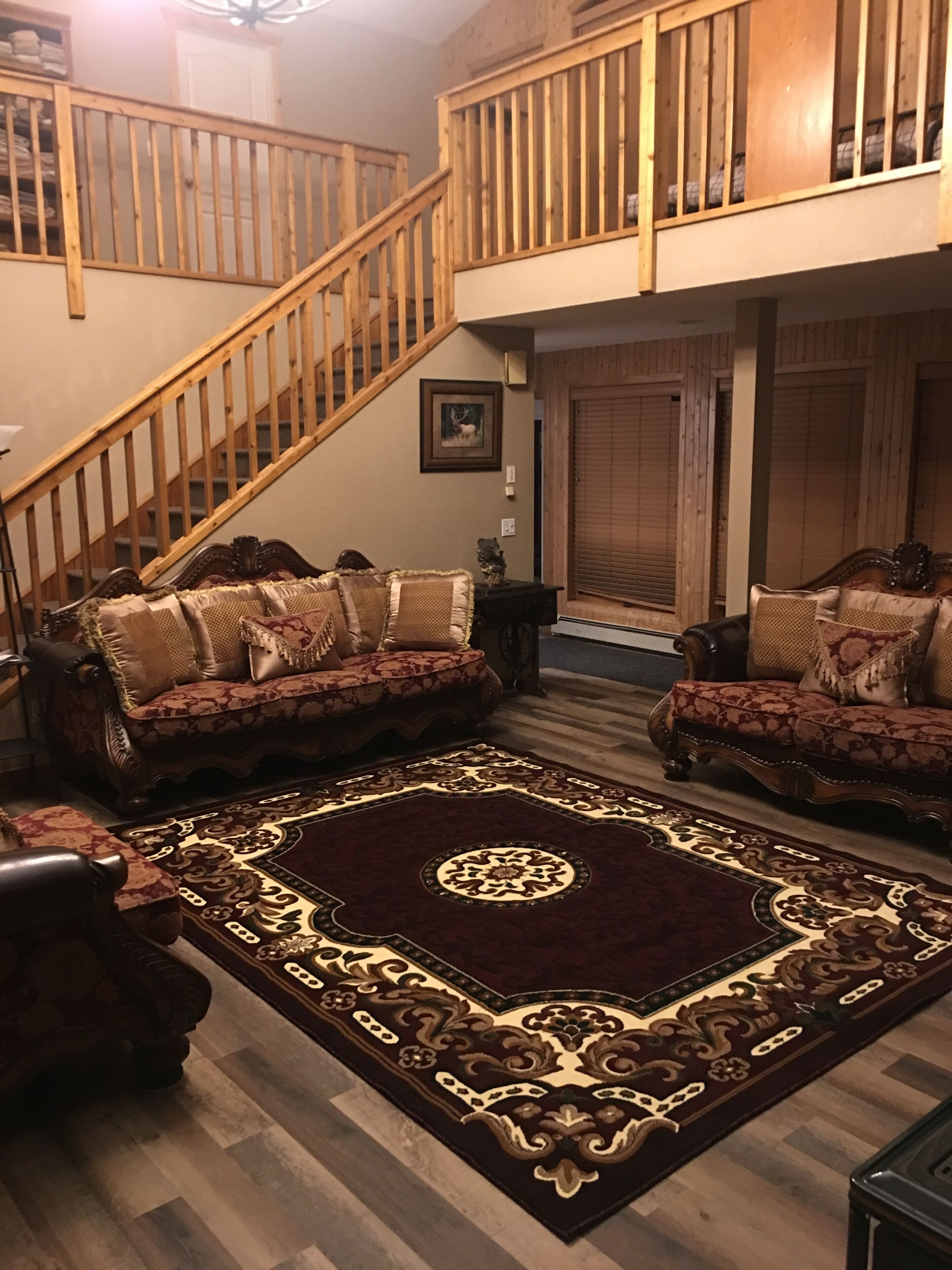 A spacious living room with a large wooden staircase, two sofas with patterned cushions, and a decorative rug.