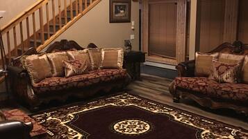 A spacious living room with a large wooden staircase, two sofas with patterned cushions, and a decorative rug.