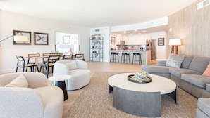 A modern living room with a grey sofa, a round coffee table, and a dining area with a table and chairs.