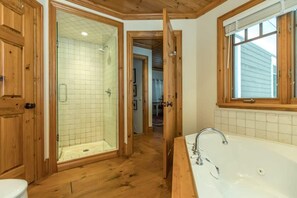 A bathroom with a glass-enclosed shower, a bathtub, wooden flooring, and wooden doors.