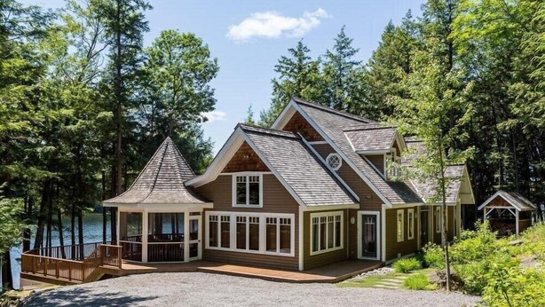 Eine Hütte mit einer großen Terrasse, mehreren Fenstern und Blick auf den umliegenden Wald.