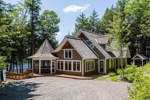 En hytte med stor terrasse, flere vinduer og udsigt over den omkringliggende skov.