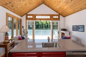 A kitchen with a central island, wooden ceiling, large windows, and a view of a deck. - Sandy Shores on Lake Joe (Minett)