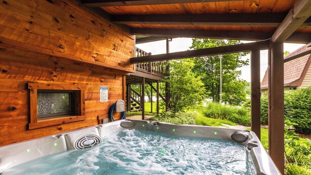 A hot tub in a wooden cabin with a view of greenery and a wooden deck.