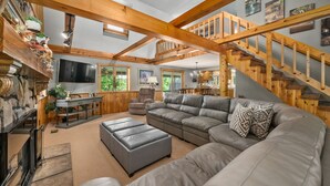 A spacious living room with a large gray sectional sofa, a fireplace, a wooden staircase, and a dining area with a table and chairs.