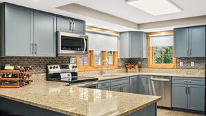 A modern kitchen with granite countertops, stainless steel appliances, and grey cabinetry.