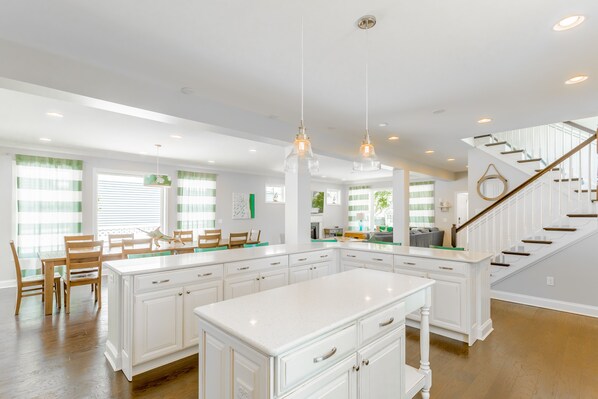 A spacious kitchen with white cabinetry, a large island, and a wooden staircase leading to an upper level.