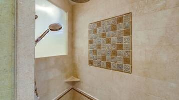 Ein Badezimmer mit beigen Fliesen, einer Duschbrause und einem dekorativen Fliesemuster an der Wand.