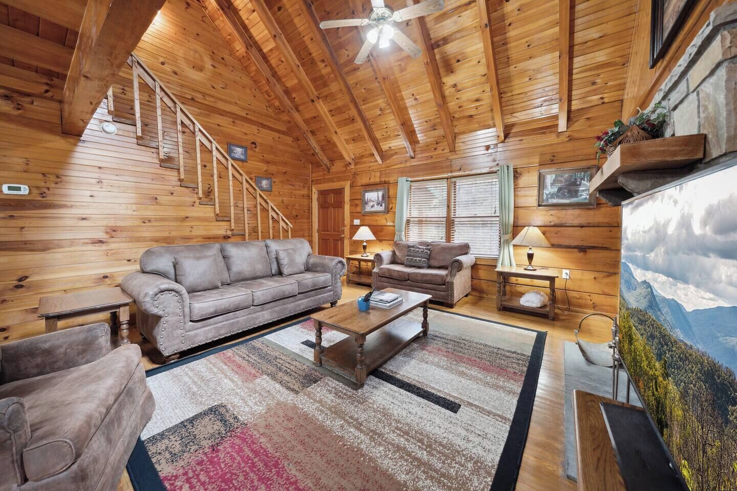 A cozy log cabin interior with a wooden ceiling, a sofa, a coffee table, and a painting of a mountain landscape.