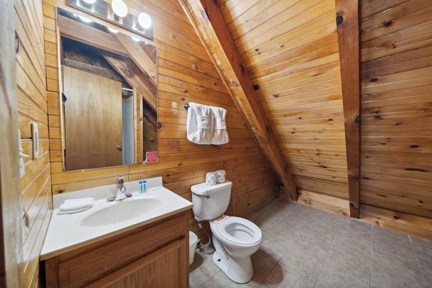 A wooden-paneled bathroom with a sink, mirror, and toilet.