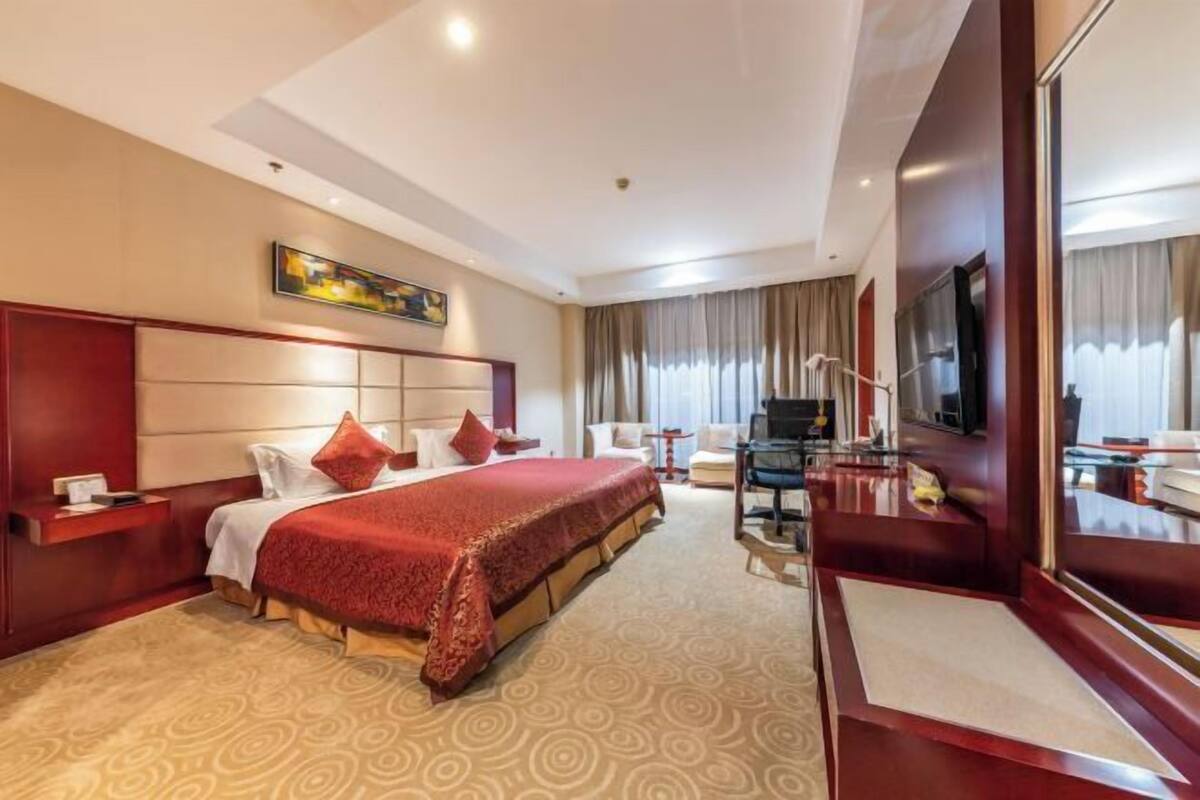 A hotel room with a large bed, a desk with a chair, a television, and a large mirror.