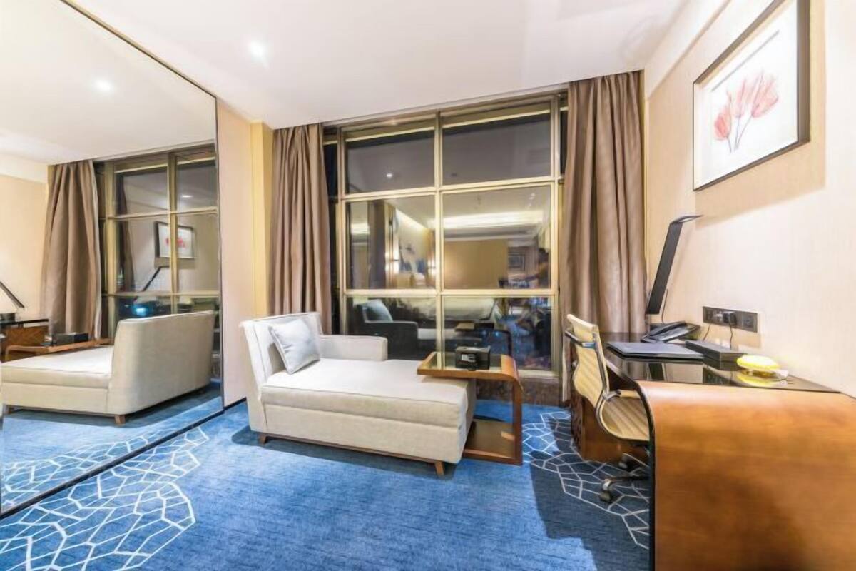 A hotel room with a large window, a sofa, a desk, and a chair.