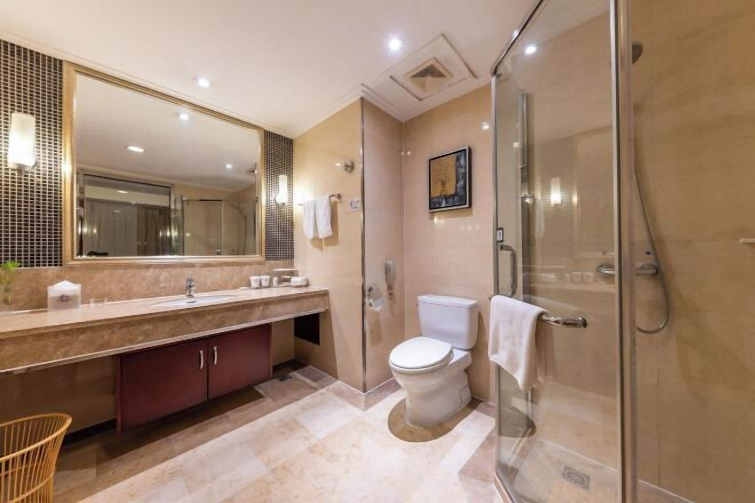 A modern bathroom with a glass-enclosed shower, a large mirror, and a marble countertop.