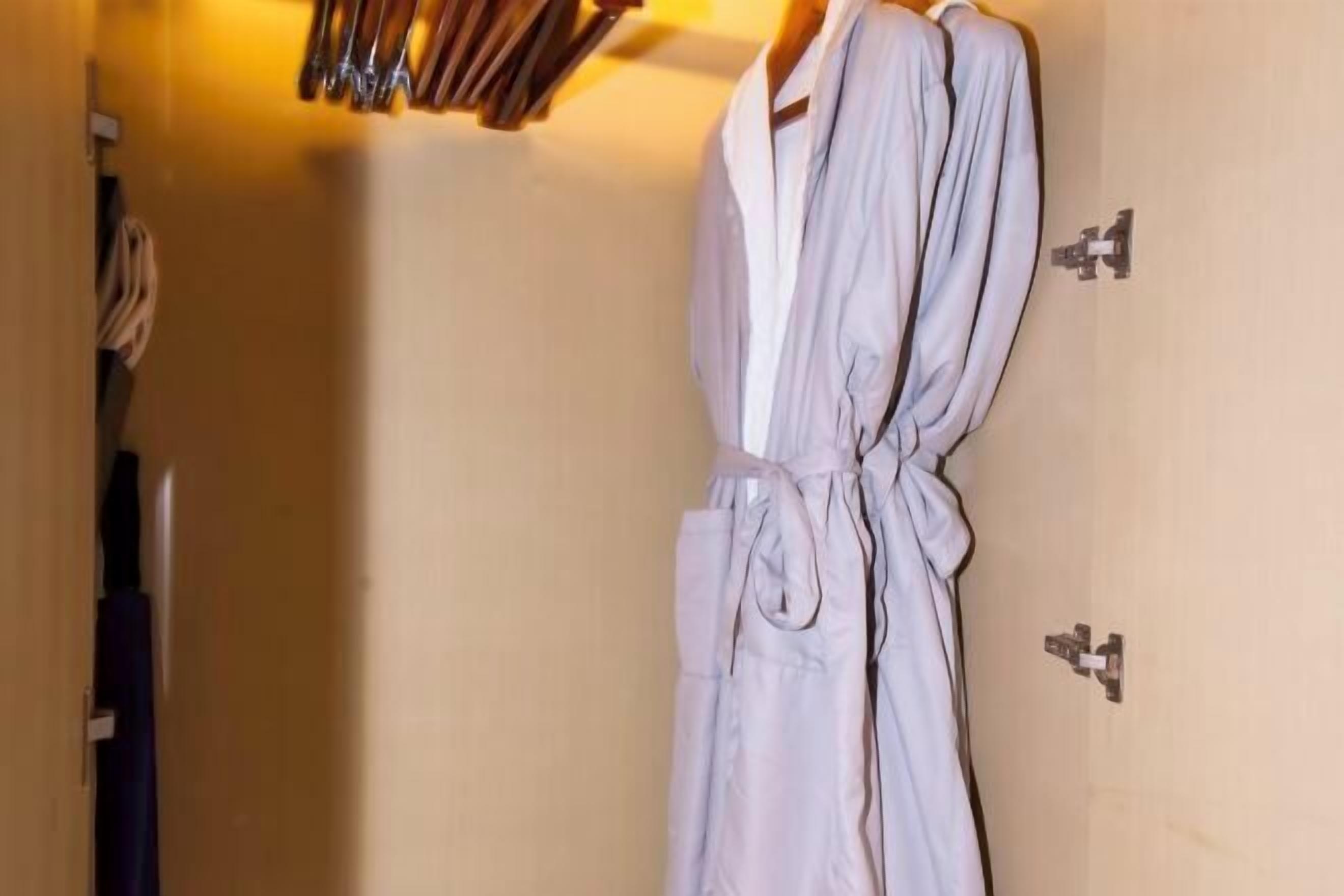 A bathroom with a white robe hanging on a rack, a towel rack, and a door with a towel hanging on it.
